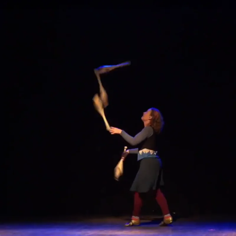 Cindy Marvell juggling clubs under a spotlight